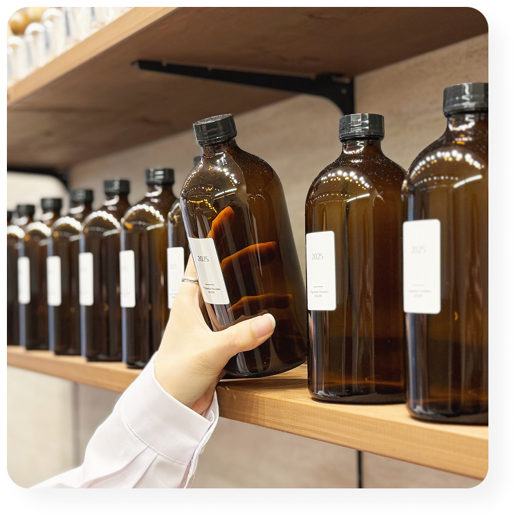 棚に並ぶ香料ボトルを手に取るスタッフの手元。