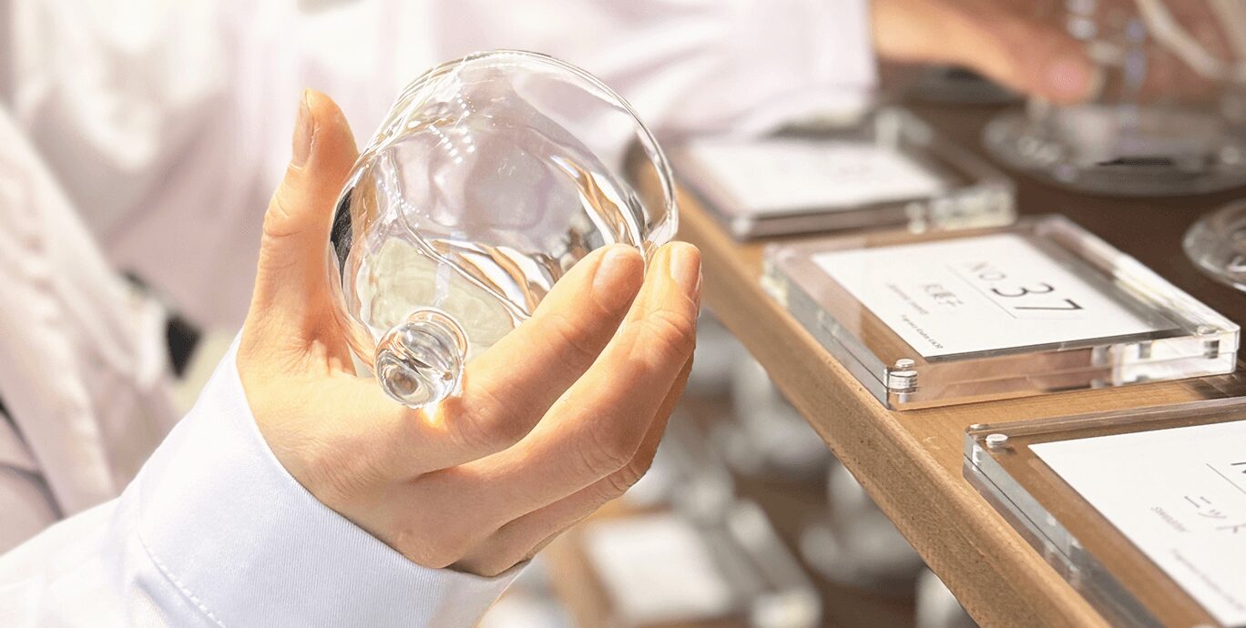 フレグランス工房「香」で香りサンプルのガラスドームを手に取る様子。香りを確かめながら選んでいる場面。